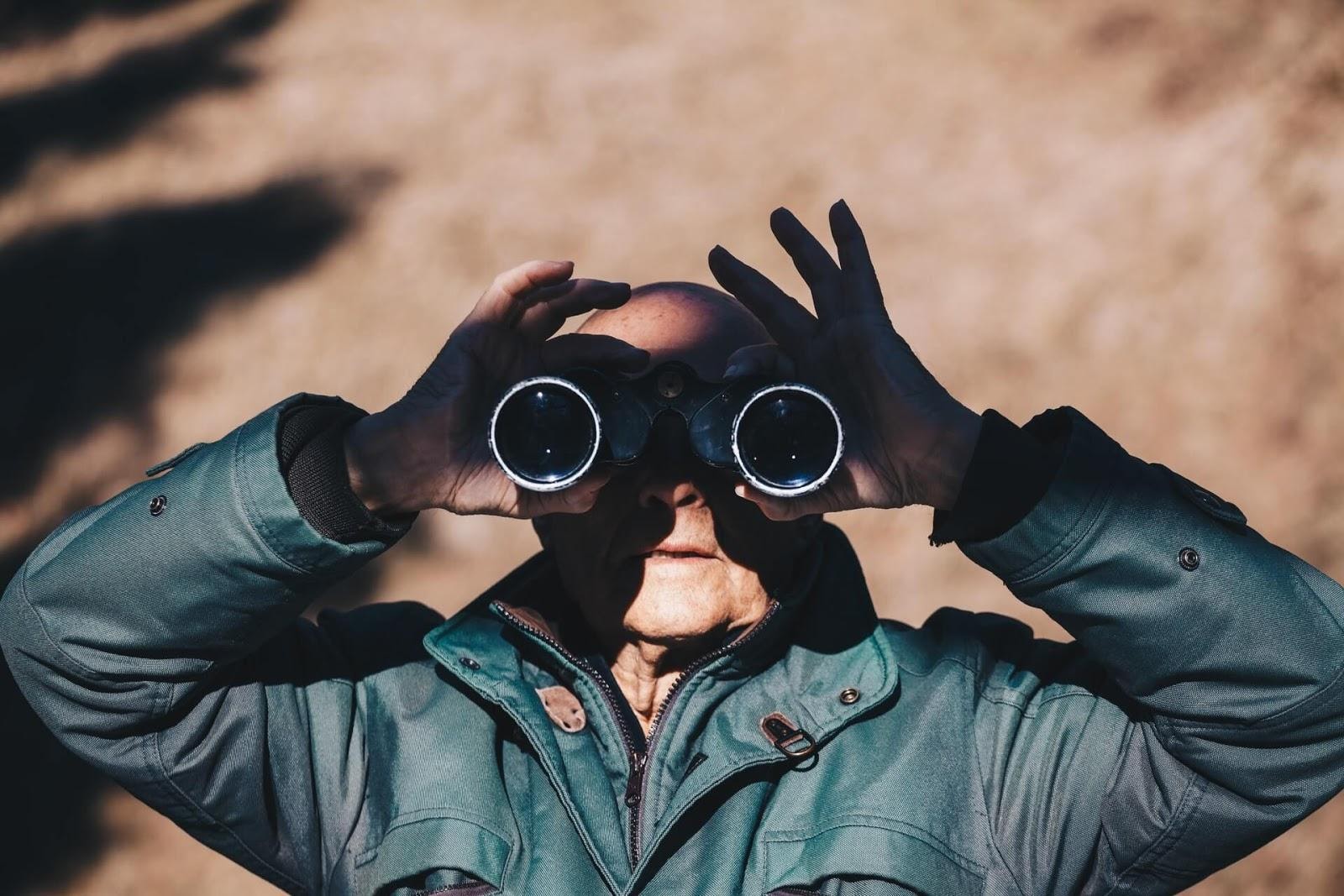 an older man in a green jacket looking through a pair of binoculars