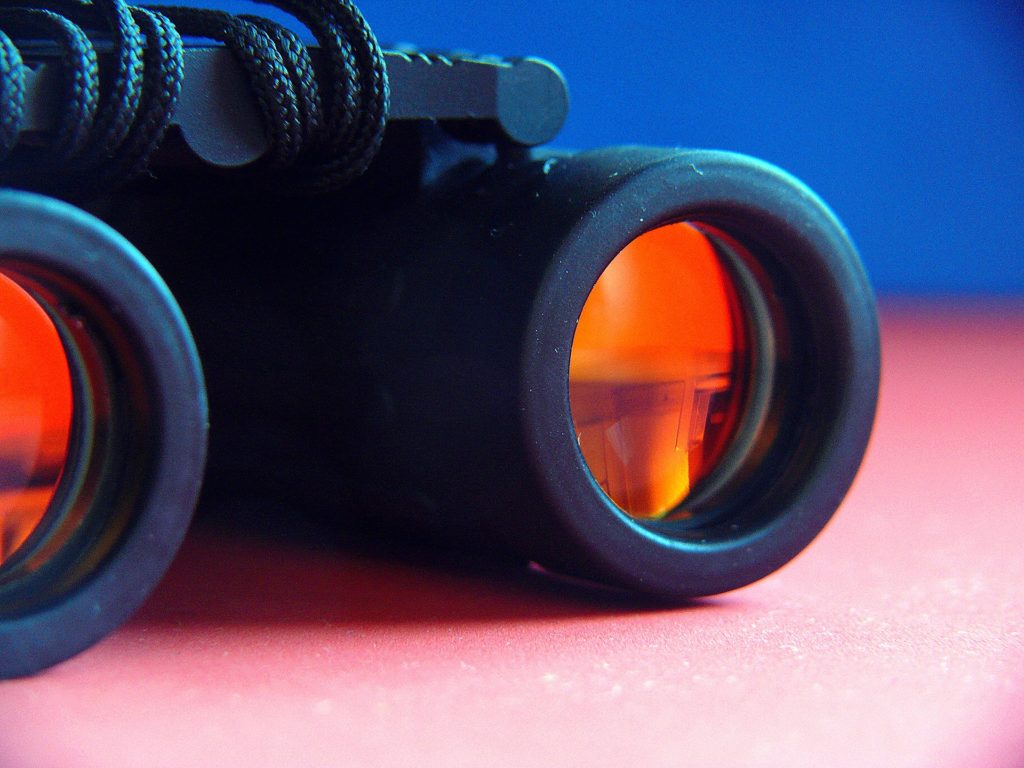 Binoculars with coated front lenses resting on a surface