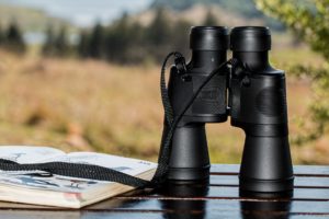 Black Porro prism binoculars on a table next to an open book