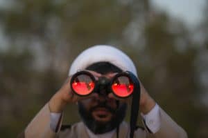 a man looking through a pair of binoculars with red light reflected in them