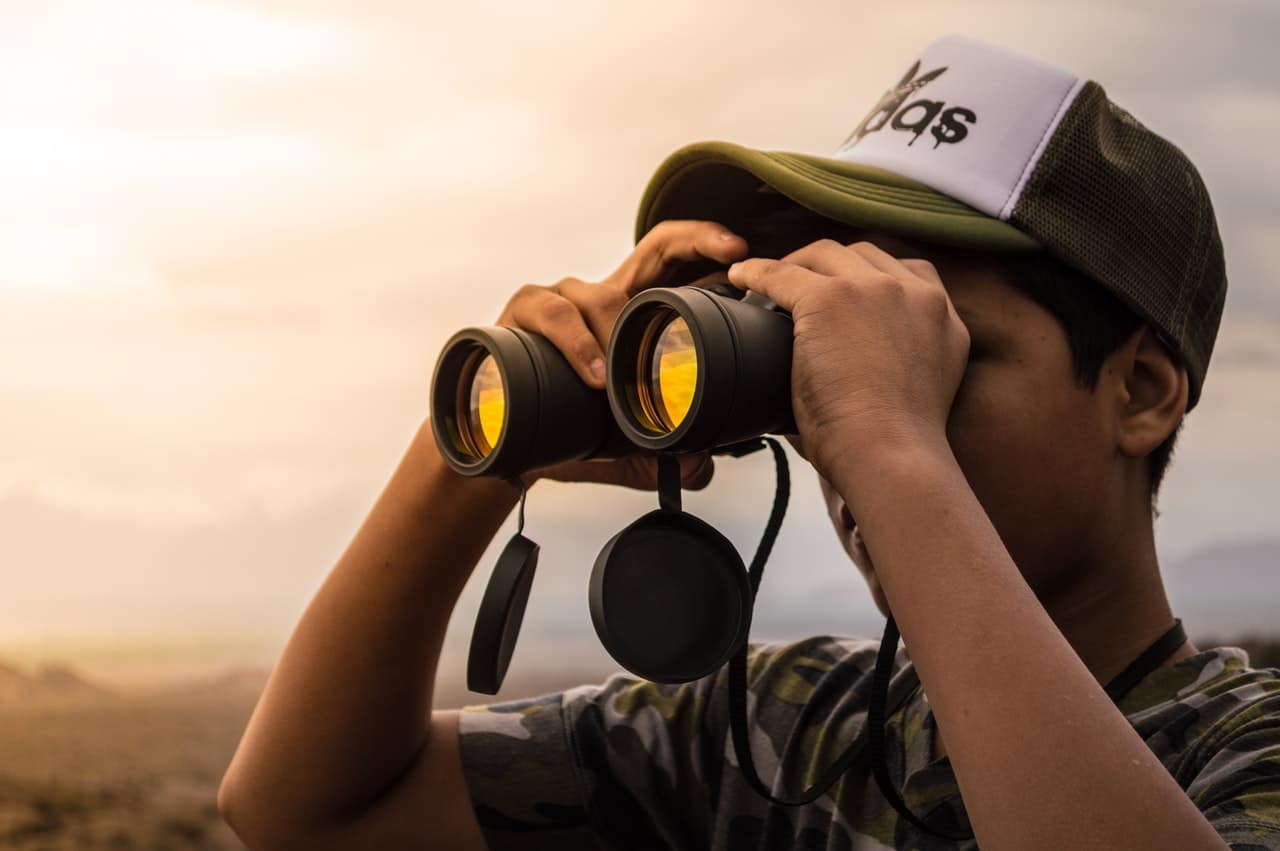 A young man wearing a cap looking through binoculars