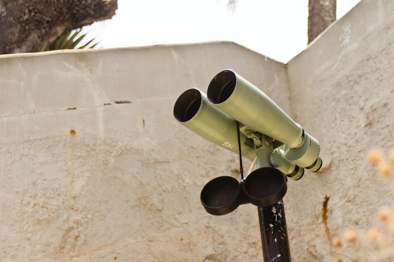 Large size roof prism binoculars mounted on a stand next to a wall