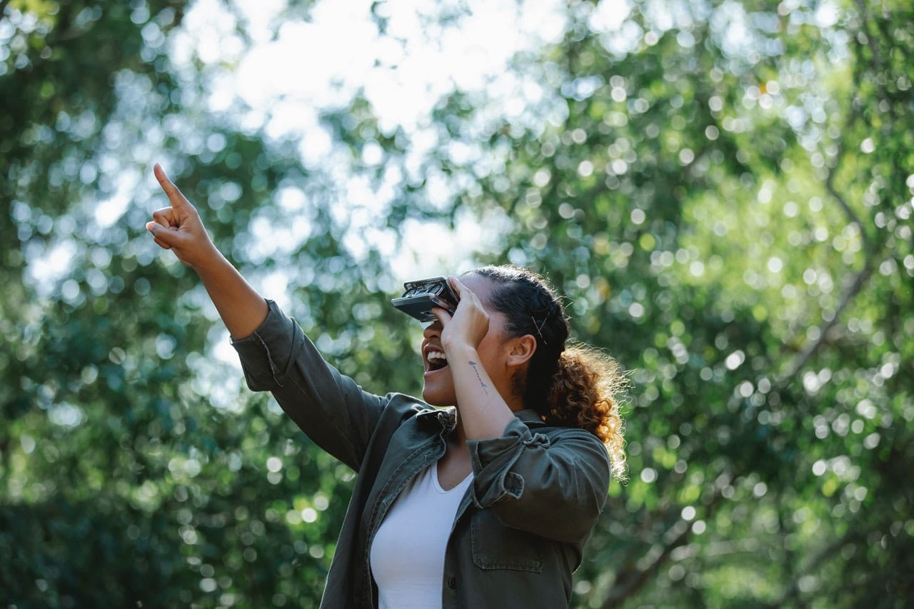 An excited lady staring through a compact binocular while pointing up 